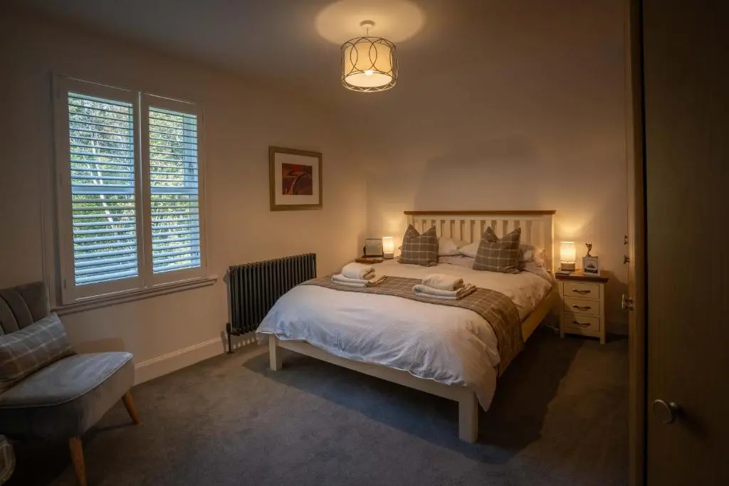 a bedroom with a bed and a chair and windows at Glen Tilt House in Bridge of Tilt