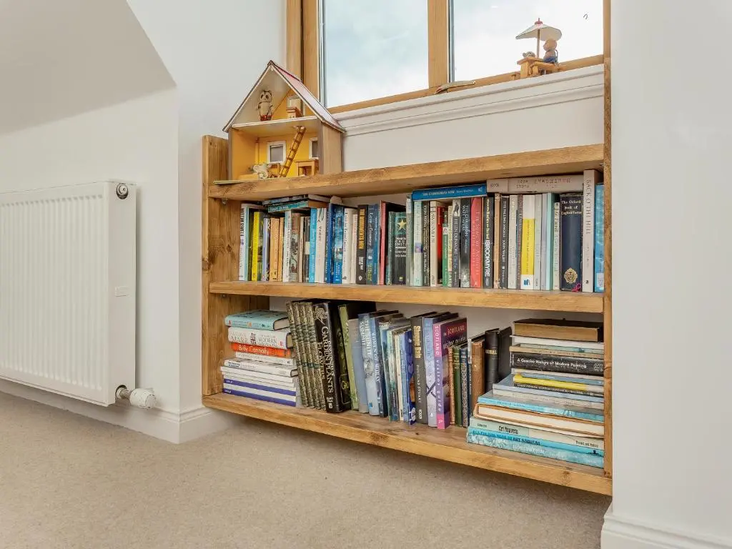 a book shelf filled with books next to a window at East Cottage in Cawdor