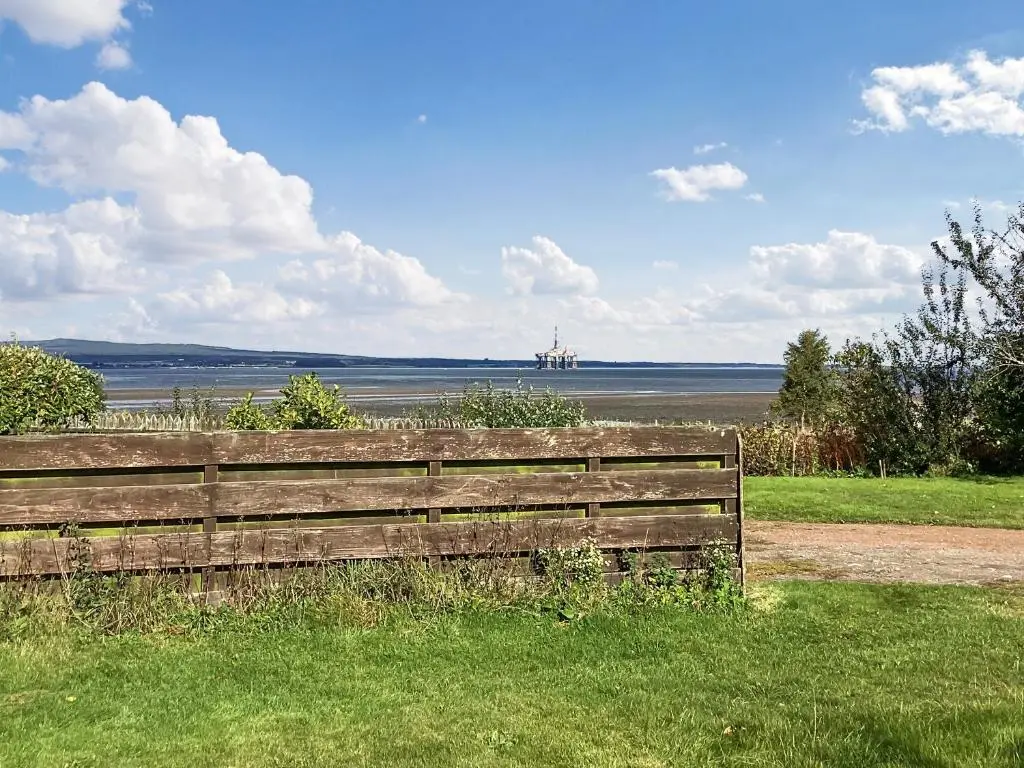 a wooden bench sitting in the grass near a body of water at Old Laurel Cottage in Jemimaville