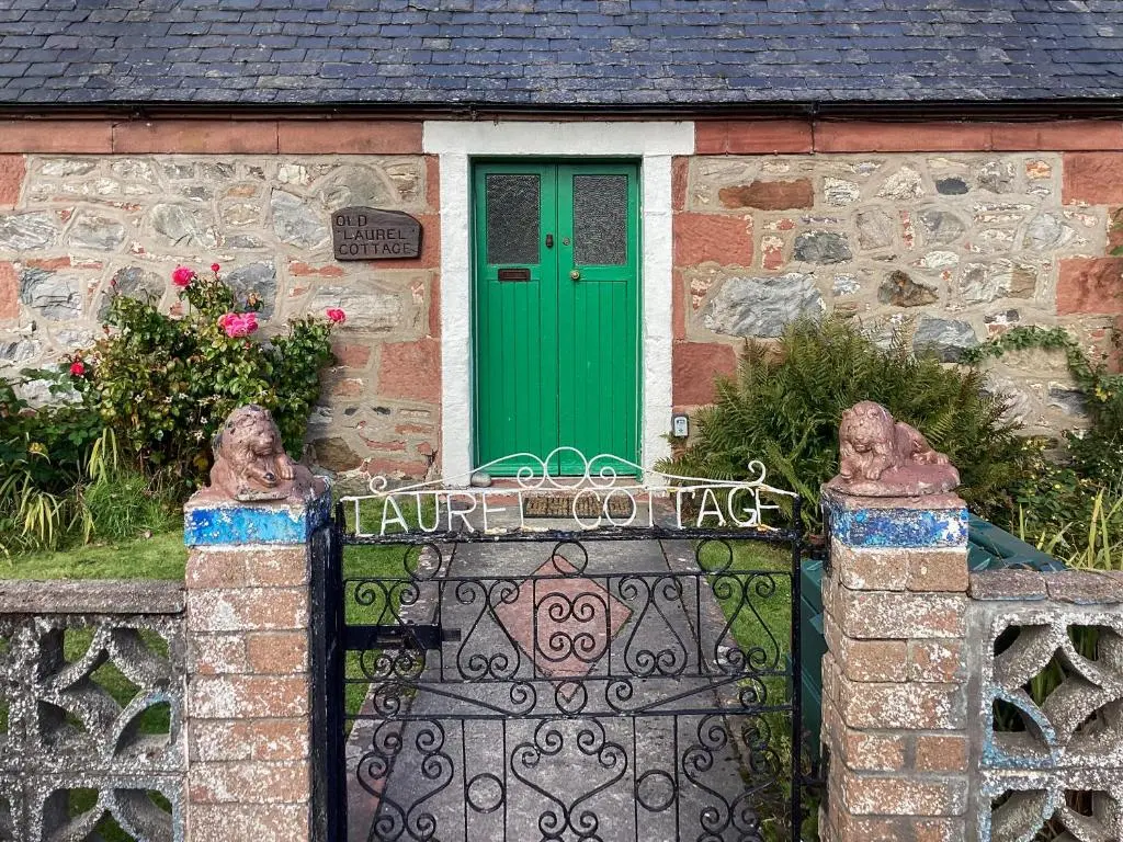 a gate in front of a stone house with a green door at Old Laurel Cottage in Jemimaville