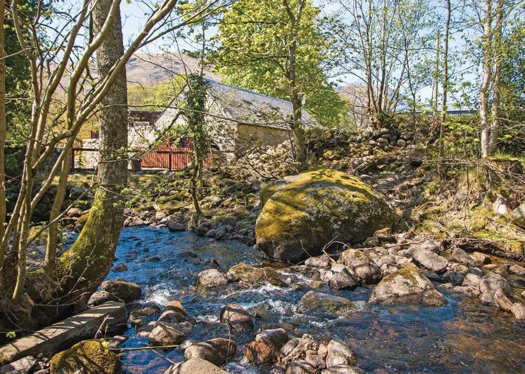 a stream with rocks and a house in the background at Glen Clova Lodges in Angus