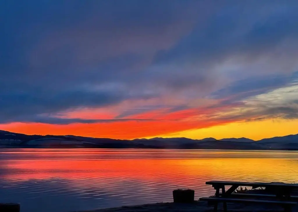a sunset over a body of water with a picnic table at Kessock Highland Lodges in Tore