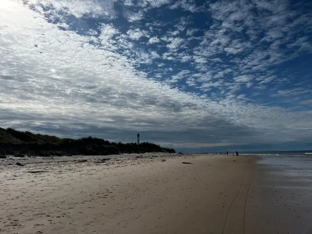a beach with people walking on the sand at Sand Dollar, Silver Sands Holiday Park in Lossiemouth
