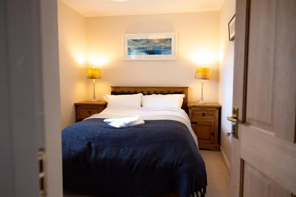 a bedroom with a bed with a blue blanket and two lamps at Wynstone Cottage, Speyside in Fochabers