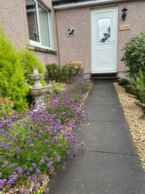 a house with a white door and purple flowers at Treetops Bungalow Loch Ness in Drumnadrochit