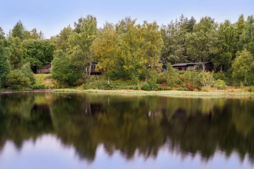 an image of a lake with houses in the background at Macdonald Lochanhully Resort in Aviemore
