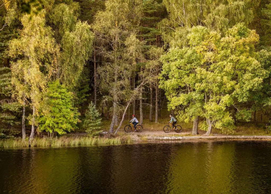 two people riding bikes next to a body of water at Macdonald Lochanhully Resort in Aviemore