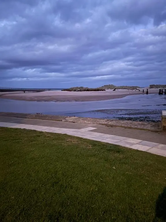 a bench on a sidewalk near a beach with water at Sutherland C14 in Lossiemouth