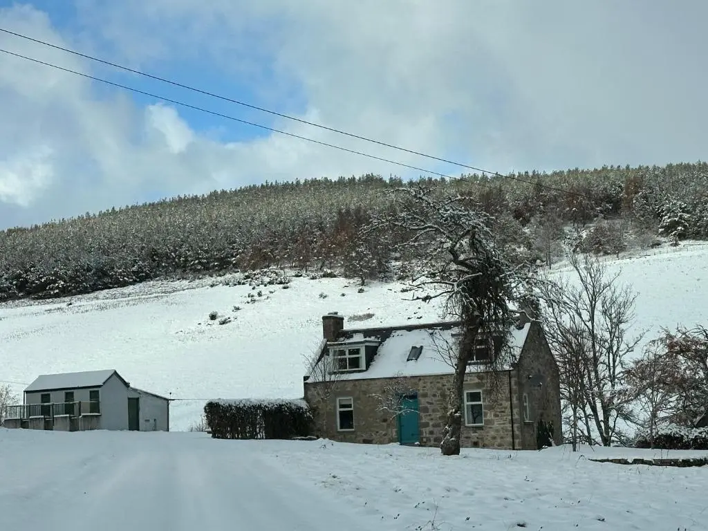 a house in the snow next to a mountain at Cosy Cottage on the Whisky Trail in Haugh of Glass