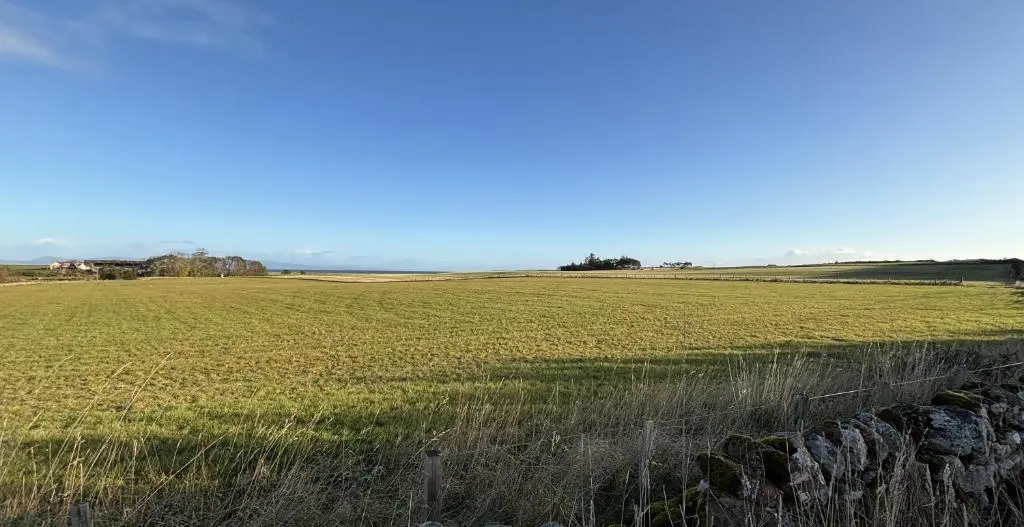 a field of grass with a fence in the foreground at Smiddy Cottage in Portmahomack