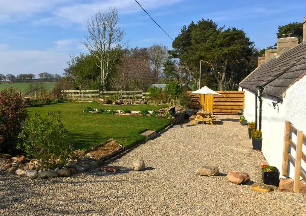a garden with a picnic table and a house at Smiddy Cottage in Portmahomack