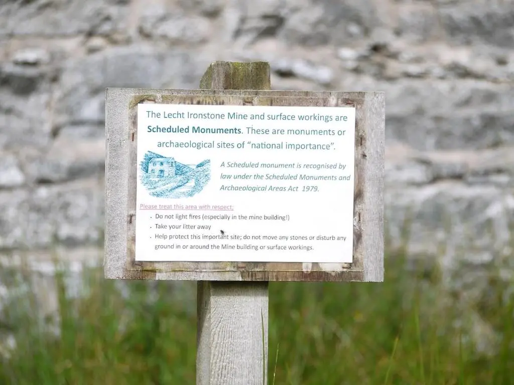 a sign on a pole in front of a stone wall at Charming cottage close to the Cairngorms in Ballindalloch
