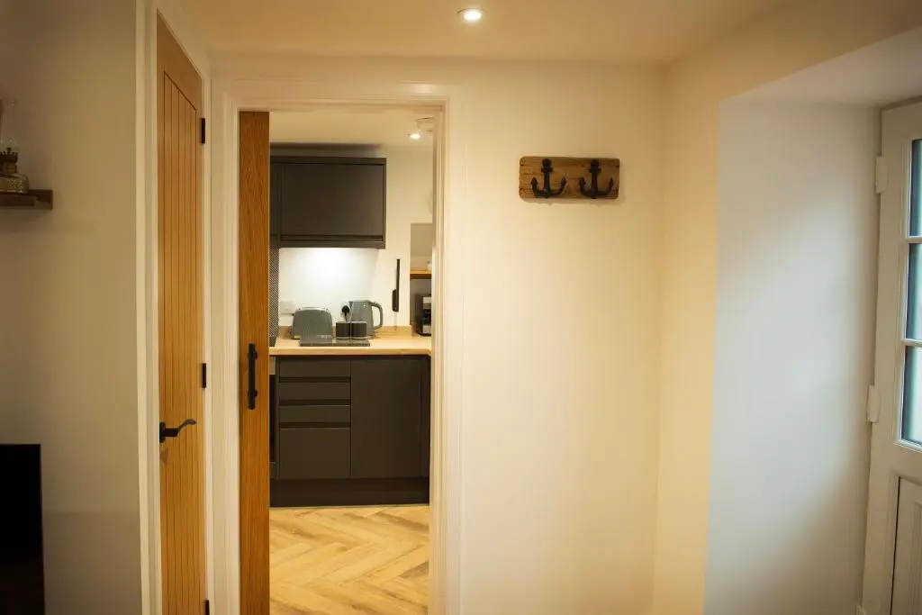 a hallway leading to a kitchen with black appliances at Coorie-In Cottage in Whitehills