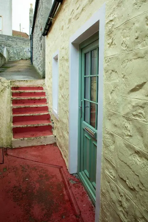 a green door on the side of a building with stairs at Coorie-In Cottage in Whitehills