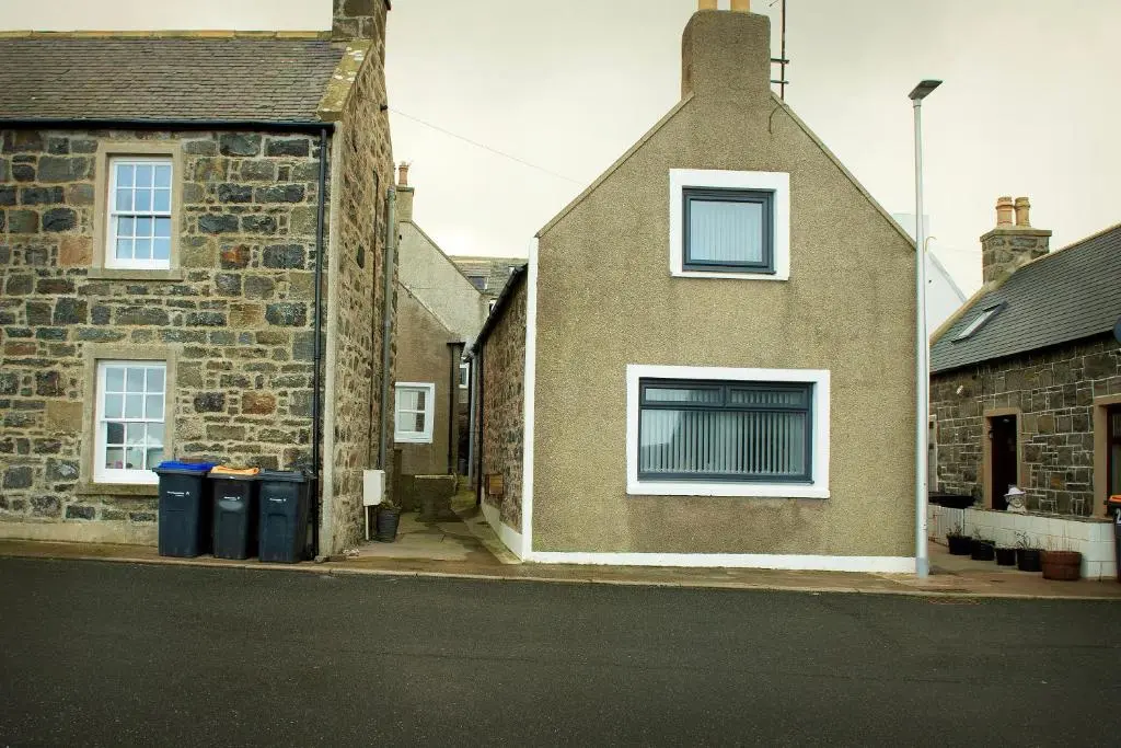 a brick house with two windows and two trash cans at Coorie-In Cottage in Whitehills
