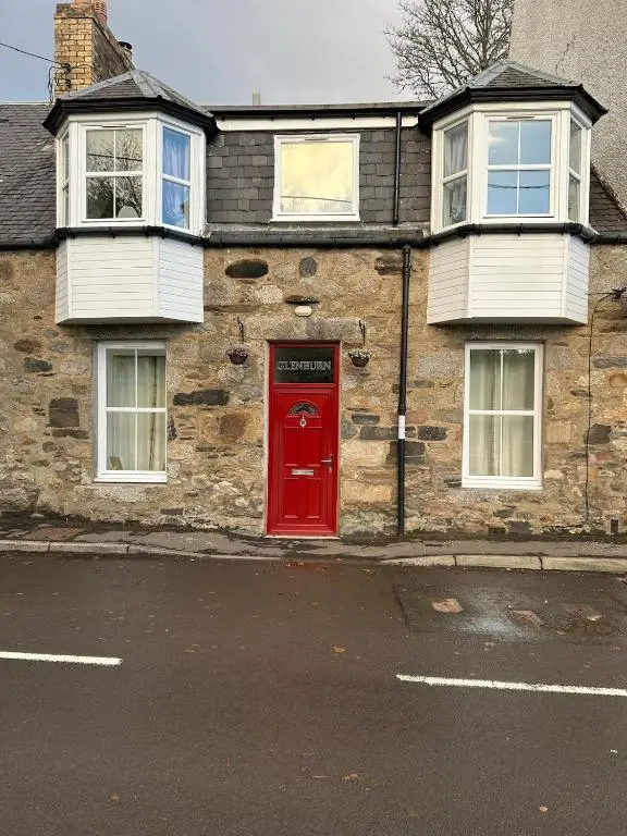 a brick house with a red door on a street at Glenburn Cottage in Kirkmichael