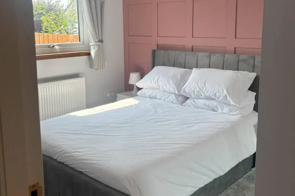 a white bed with a pink headboard and white pillows at The Burghead Hideaway in Burghead
