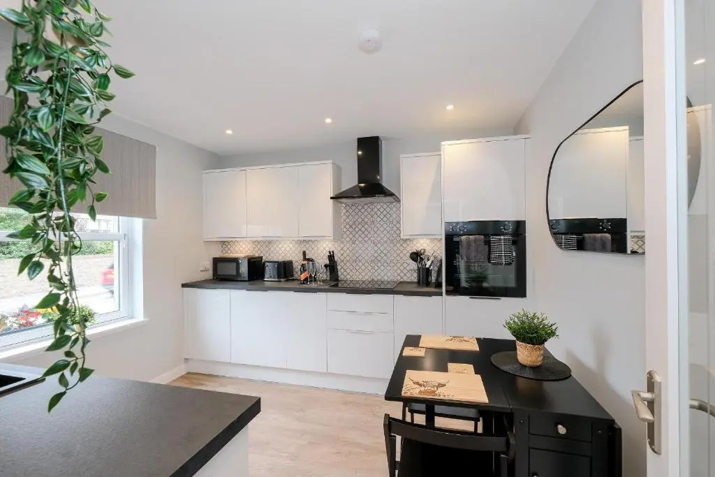 a kitchen with white cabinets and a black table at High Street Retreat in Inverurie