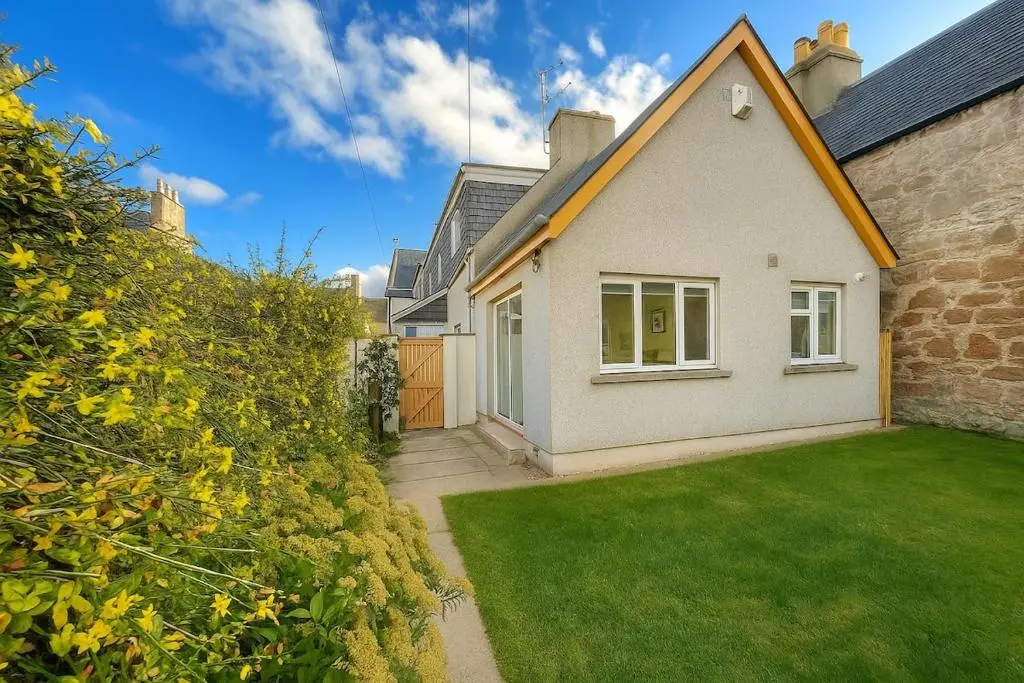 a white house with a green lawn in front of it at Beachy Days and Family Stays in Nairn