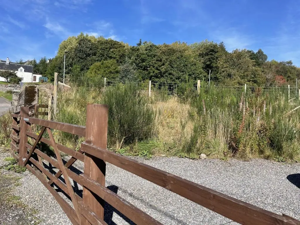 a wooden fence next to a field of tall grass at Culrain Cottage in Fort Augustus