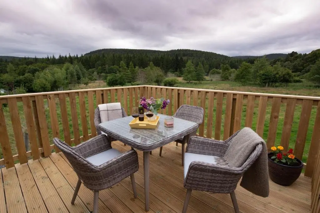 a wooden deck with a table and chairs on it at Beautiful dog friendly lodge with hot tub in Aboyne