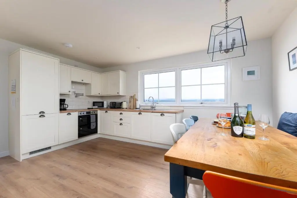 a kitchen with white cabinets and a wooden table at Linden House in Fortrose