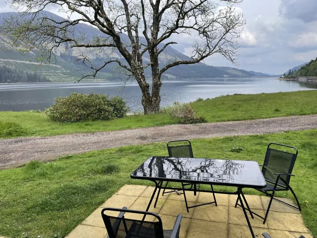 a table and chairs sitting next to a lake at Mountain Thyme Lodge in Kilfinnan