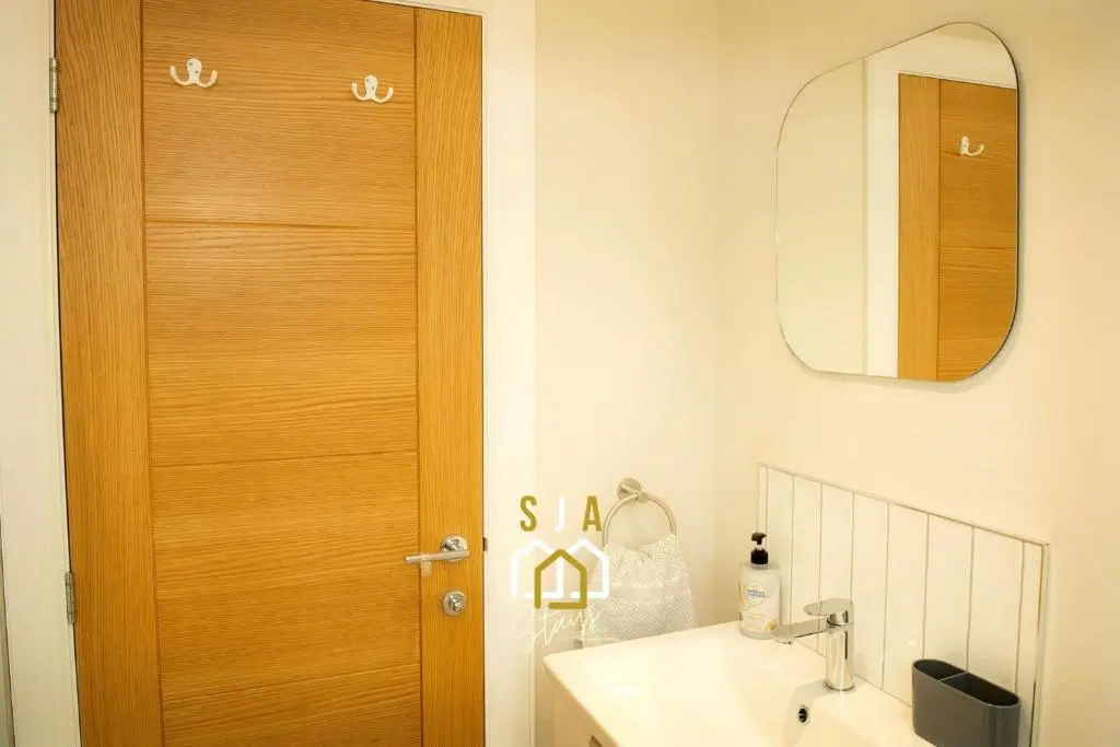 a bathroom with a wooden door next to a sink at Beachside Cottage - SJA Stays - Modern 3 Bedroom House in Cullen
