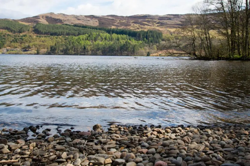 a rocky shore of a lake with mountains in the background at Raven Wing 17 - Aonach Mor in Fort Augustus