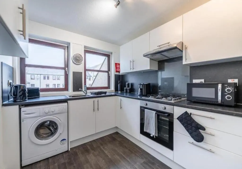 a kitchen with white cabinets and a washer and dryer at Bright & Spacious 2BR Fraserburgh for Work & Family Stays in Fraserburgh