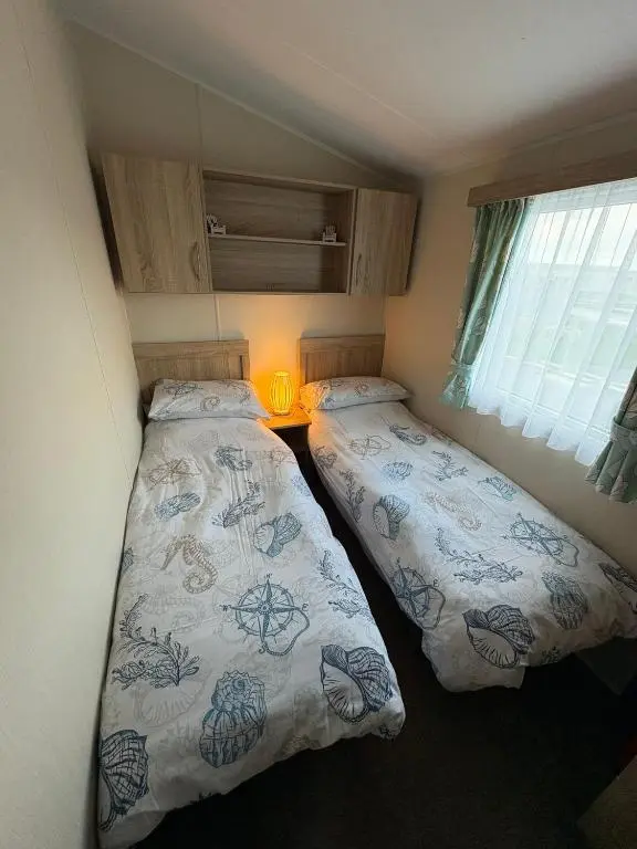 two beds in a small bedroom with a window at Pebble Cove 74 in Lossiemouth