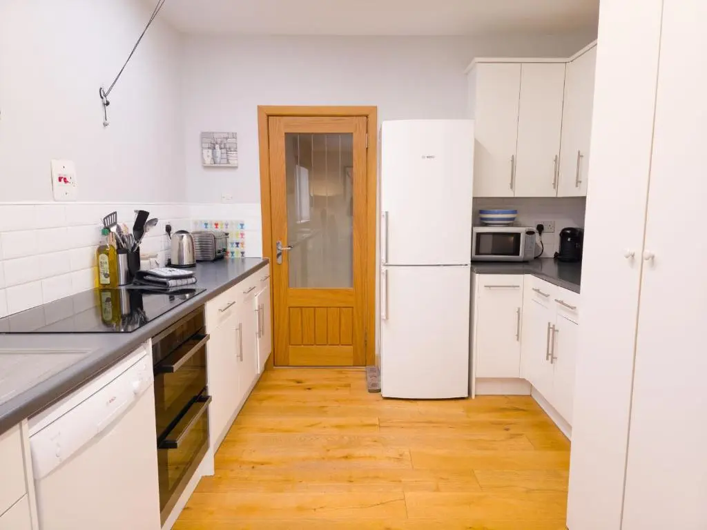 a kitchen with white cabinets and a wooden door at Loramore in Aviemore