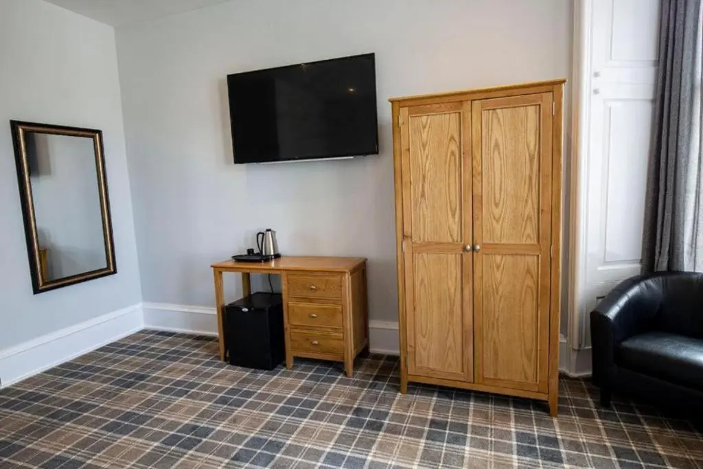 a living room with a television and a wooden cabinet at Crown Hotel & Bar in Inverness