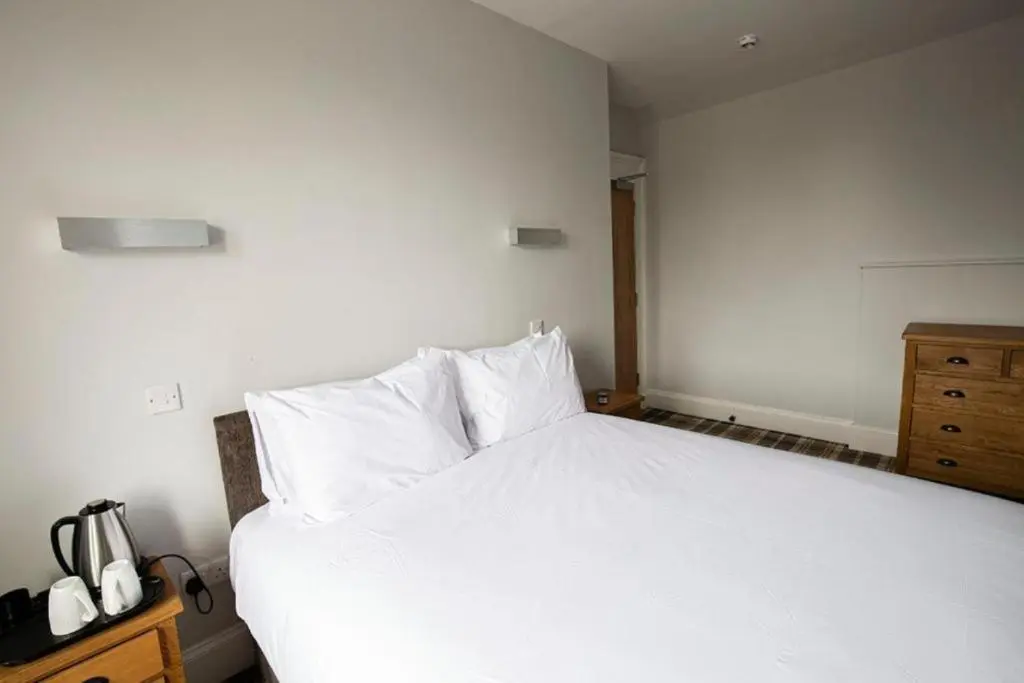 a bedroom with a white bed and a wooden dresser at Crown Hotel & Bar in Inverness