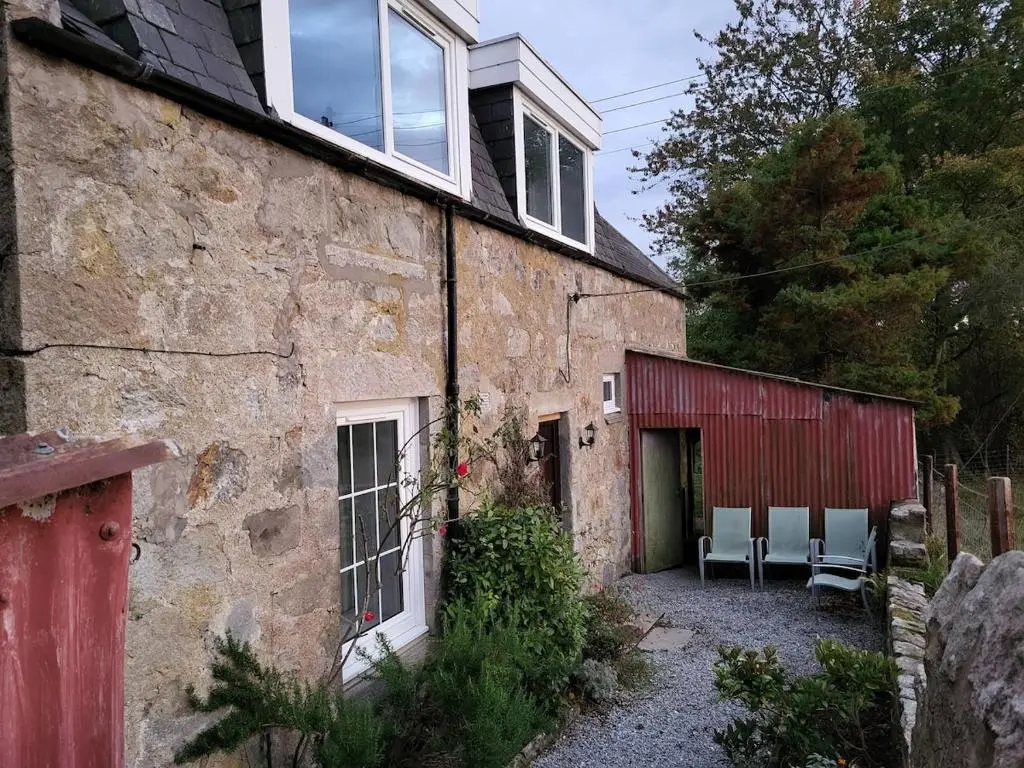 an old stone house with chairs and a red building at Gardeners Cottage