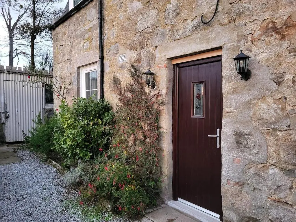 a brown door on a stone building with a bush at Gardeners Cottage