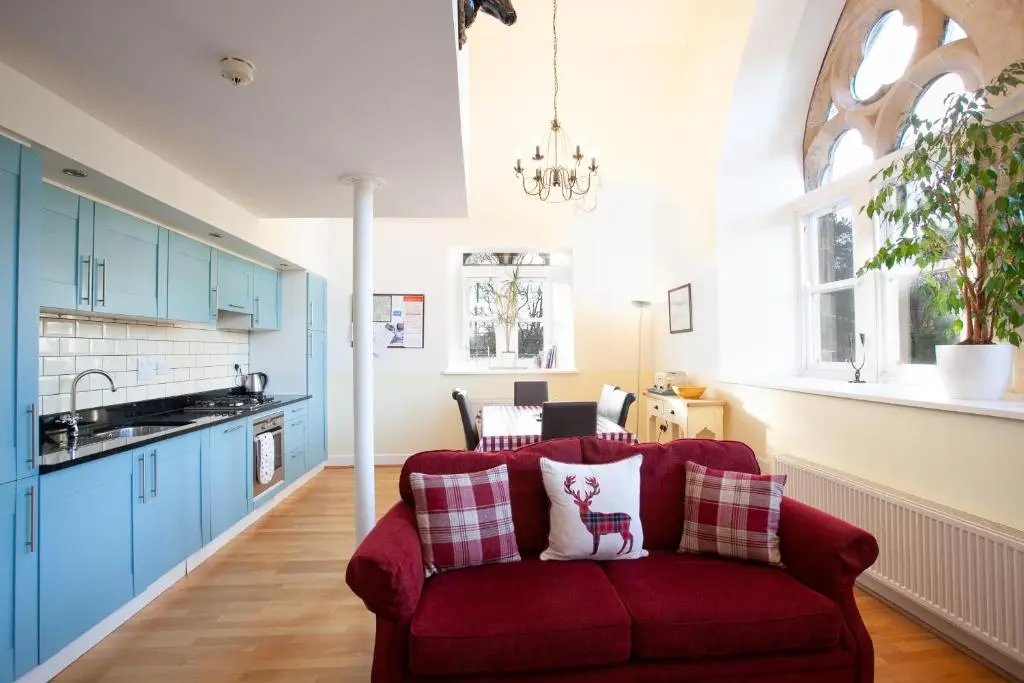 a red couch in a kitchen with blue cabinets at Old School Apartments Highland Club in Fort Augustus