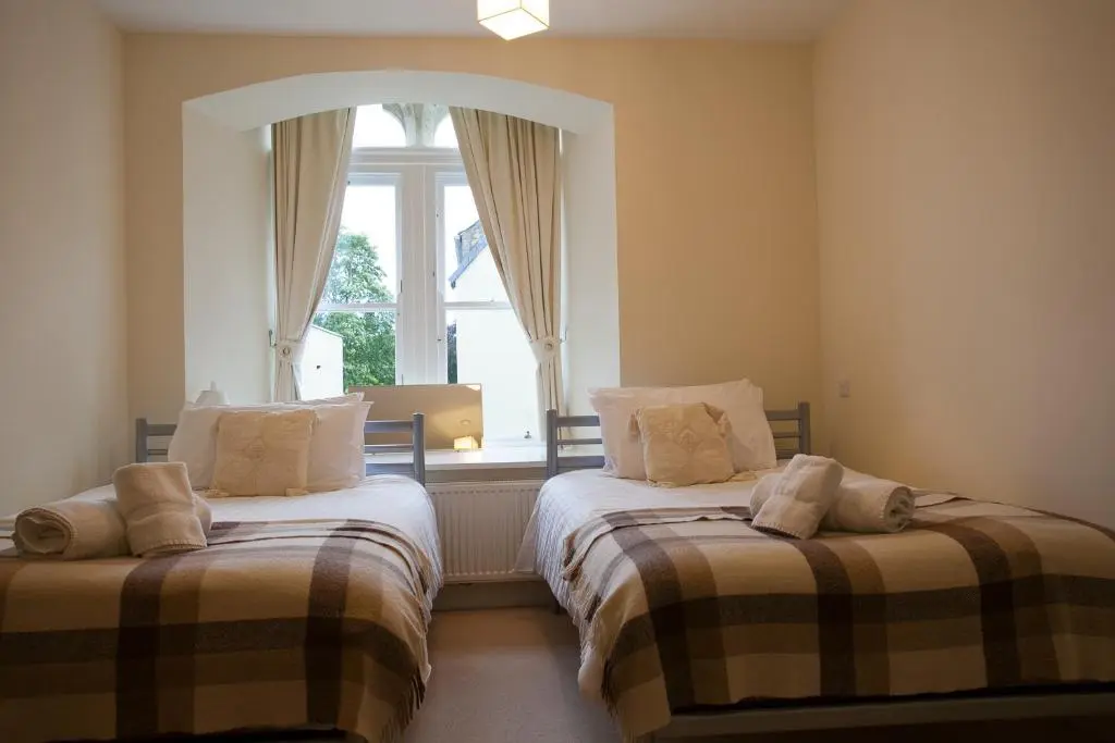 a bedroom with two beds in front of a window at Old School Apartments Highland Club in Fort Augustus