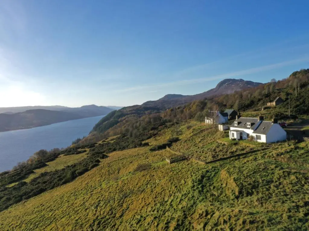 a house on top of a hill next to the water at Holiday Home Bunloit Farmhouse by Interhome in Drumnadrochit