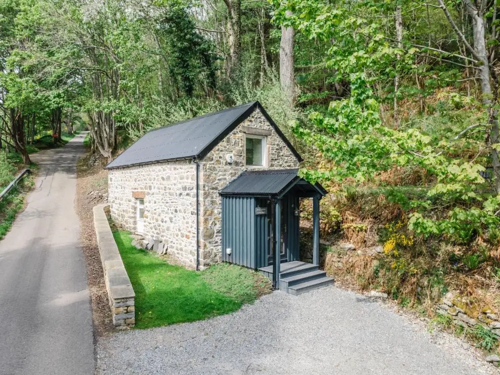 a small building with a black roof on a road at Holiday Home Wayside Bothy by Interhome in Drumnadrochit