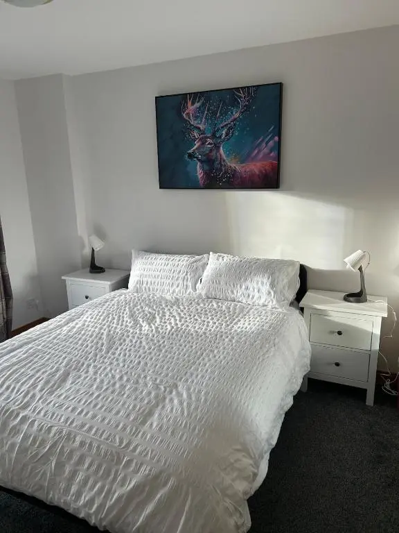 a bedroom with a white bed with a picture on the wall at Helen's Hoose in Aviemore