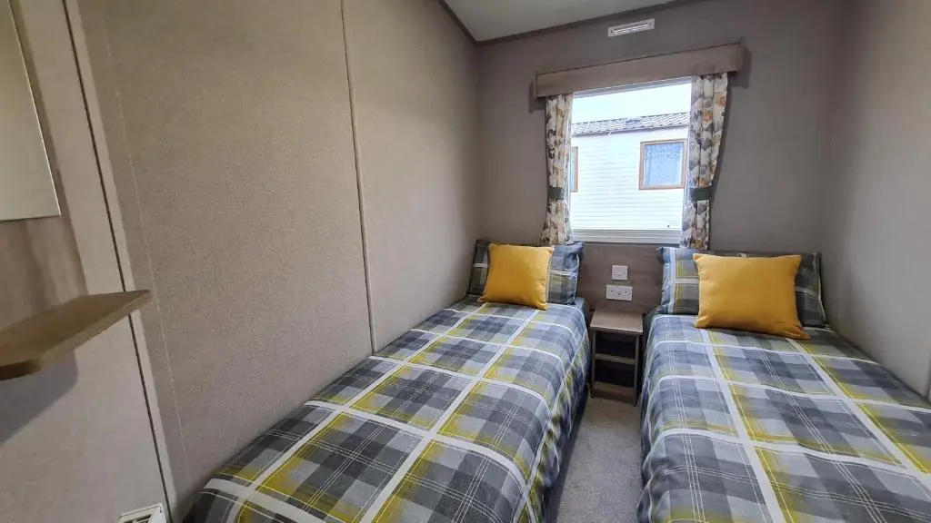 two beds in a small room with yellow pillows at Silversands - Private Caravan Let in Lossiemouth
