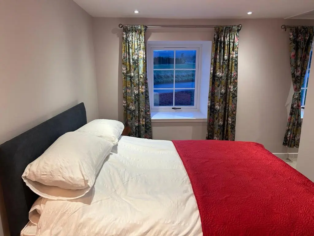 a bedroom with a bed with a red blanket and a window at Calsie Cottage, Clatt in Kirktown of Clatt