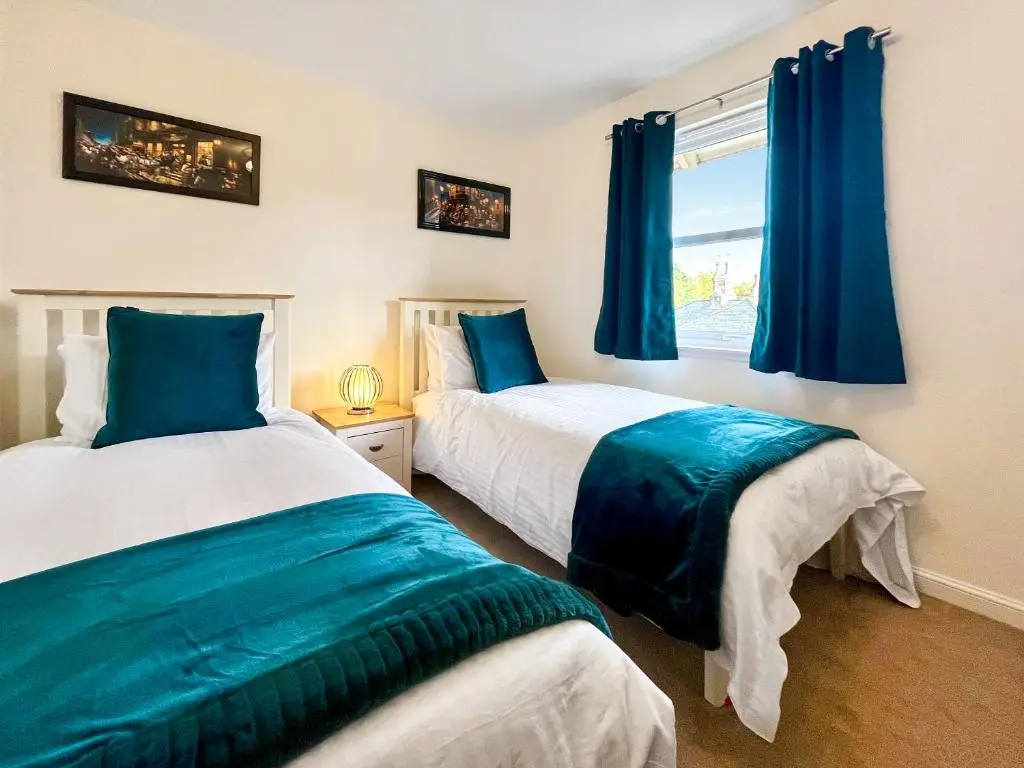 two beds in a bedroom with blue curtains and a window at Dee View Apartment in Banchory