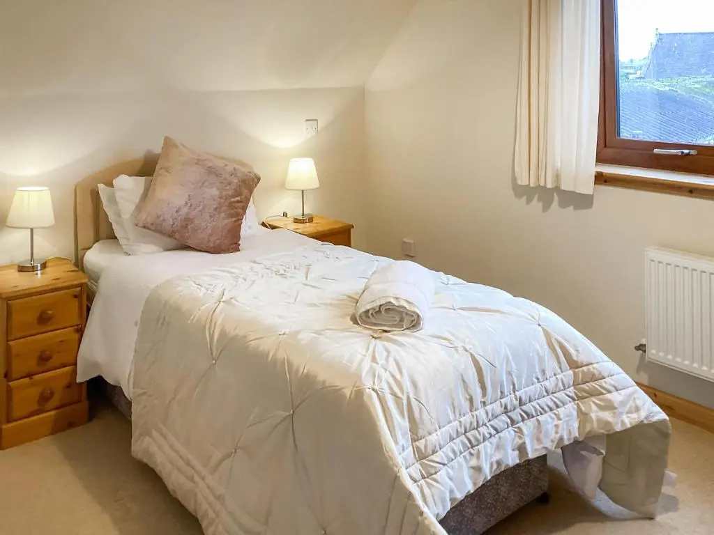 a bedroom with a bed with white sheets and a window at Mirodon in Brora