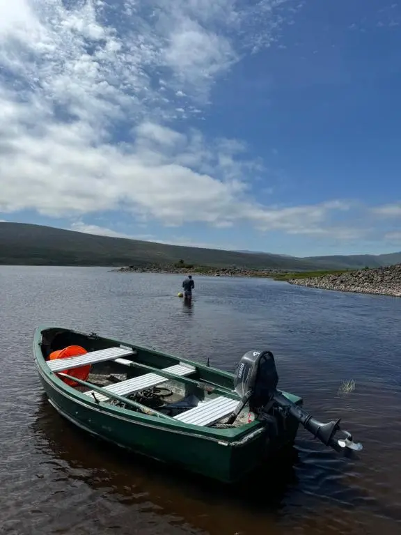 a man standing in the water next to a green boat at Overscaig House in Lairg