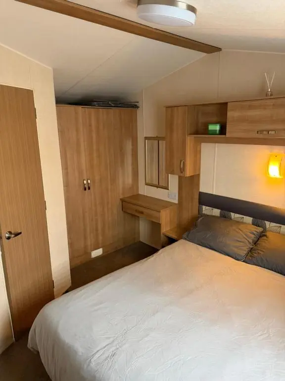 a bedroom with a white bed and wooden cabinets at Casa MALC Caravan in Lossiemouth