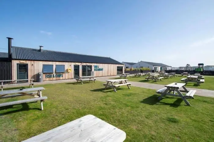 a group of picnic tables in the grass in front of a building at Casa MALC Caravan in Lossiemouth