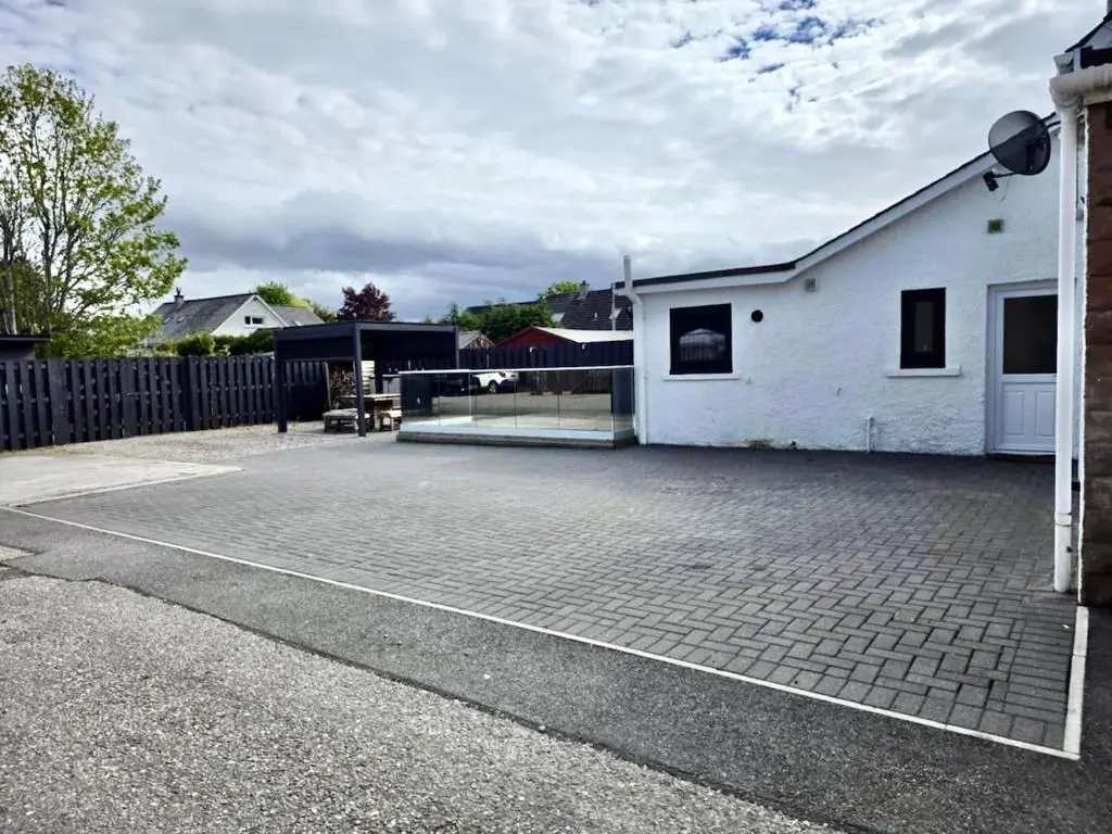 a brick parking lot with a white building and a fence at City Centre 3 Bedroom house with parking in Dalneigh