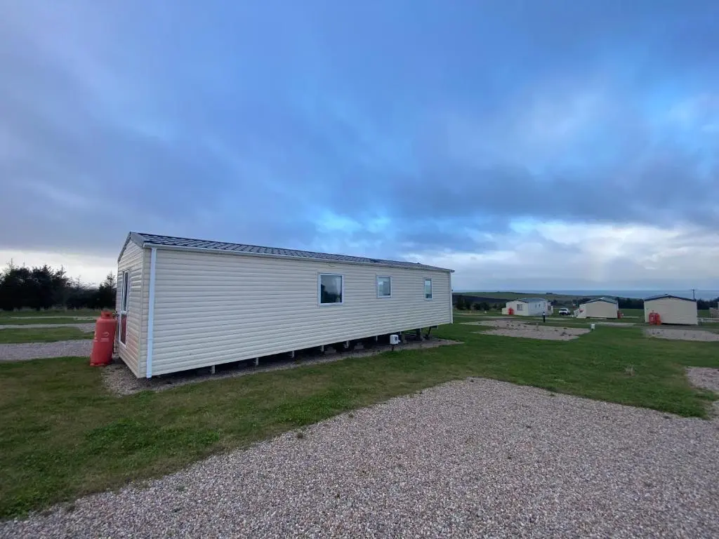 a large white building in a field with a yard at No 56 Headiton Caravan Park in Banff